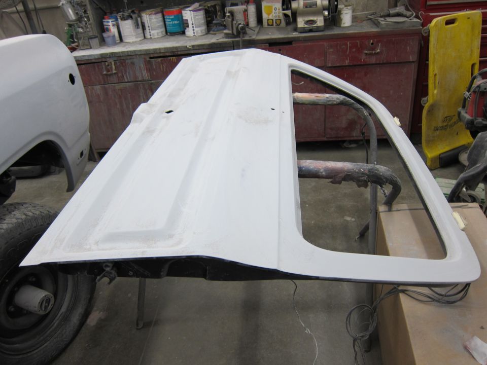 White car door on a stand, showing primer and bodywork in a garage setting