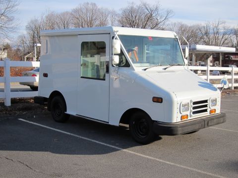 1991 Ford LTD Crown Victoria - Three-quarter front view of a plain white Grumman LLV mail-style step van parked in an asphalt lot on a bare-tree winter day, right-hand dr…