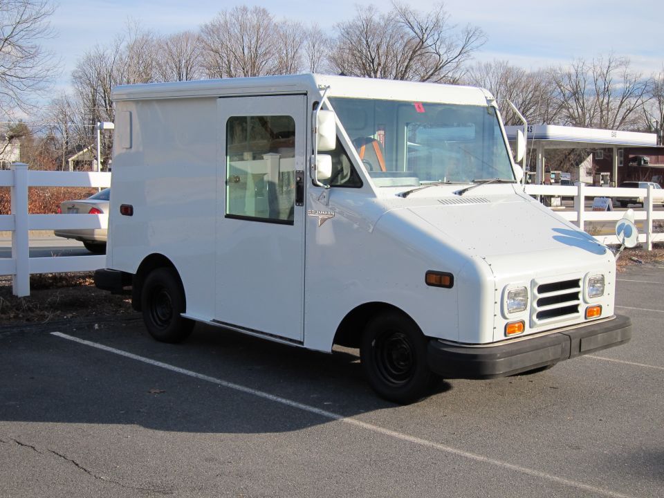 White Grumman LLV step van, right-hand drive with open sliding door, in a parking lot