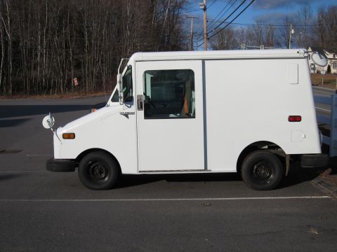 1991 Ford LTD Crown Victoria - A white Grumman step van (LLV-style delivery vehicle) shown in left-side profile, parked in an asphalt lot with bare trees behind. It has b…