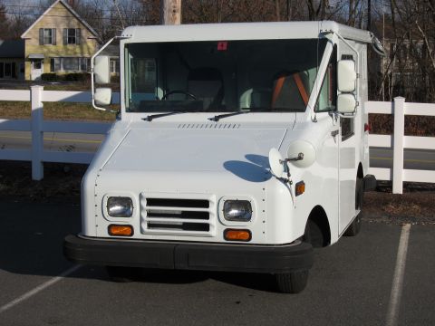 1991 Ford LTD Crown Victoria - A white boxy step van / walk-in delivery truck photographed from the front, parked on asphalt with a white fence, road, and houses in the b…