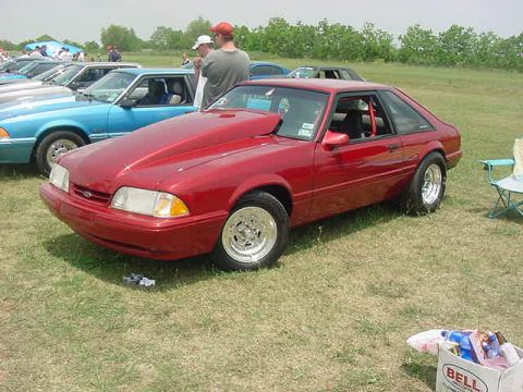 1988 Ford Bronco - A red coupe with a prominent hood scoop is parked on a grassy field, with other vehicles in the background.