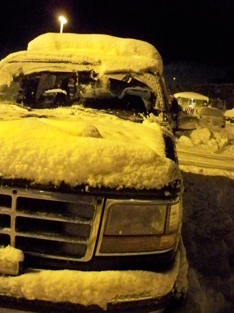 1994 Ford Bronco - A dark colored Ford Bronco is covered in snow, with other vehicles visible in the background.