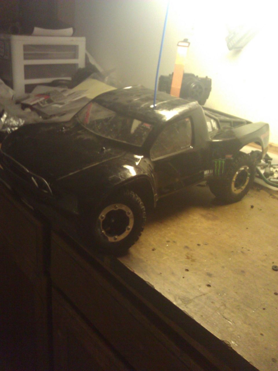 Black RC short-course truck with Monster decals on a wooden table indoors
