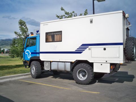 1994 Ford Bronco - This custom camper truck features a blue cab and a white living module with a spare tire mounted at the rear.