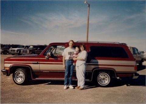 1994 Ford Bronco - A family poses in front of their red and tan SUV, with other vehicles parked behind them.