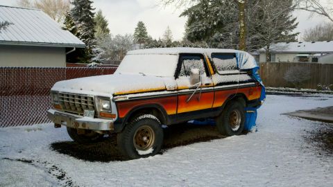 1979 Ford Bronco - A classic Ford Bronco sits in the snow, partially covered by a blue tarp.