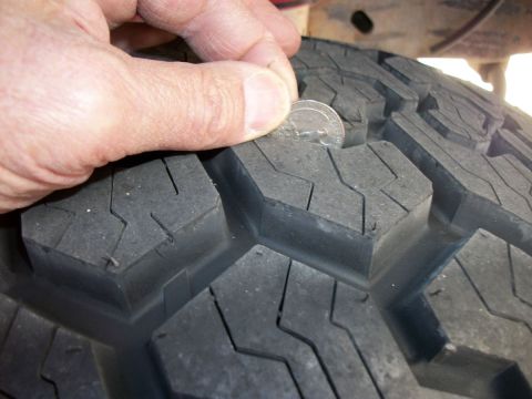 1996 Ford Bronco - A hand uses a quarter to check the tread depth on a vehicle tire.