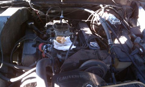1979 Ford Bronco - The engine bay of a vehicle, a carburetor and V8 valve covers. Visible text includes 'CAUTION FAN'.