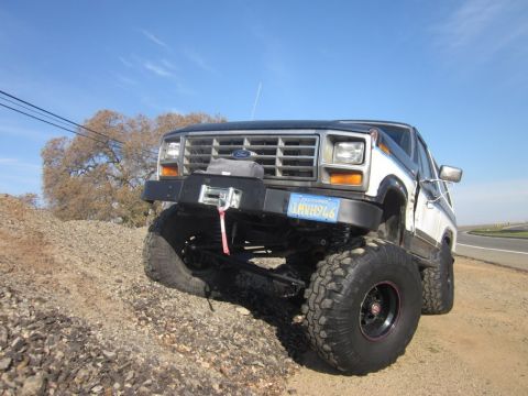 1985 Ford Bronco - This modified Ford truck is shown off-road with a clear blue sky above.