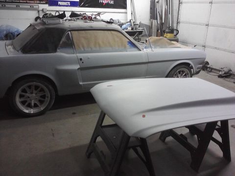 1966 Ford Mustang - A classic car is undergoing body work in a garage, with its hood removed and placed on a stand.