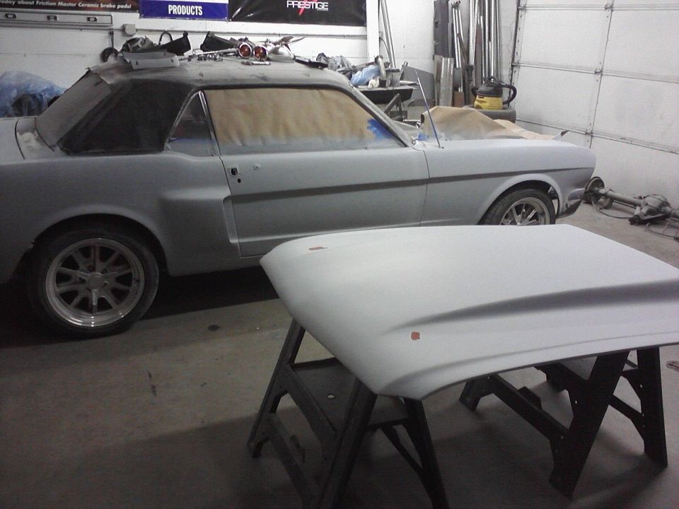 1966 Ford Mustang coupe in body shop, prepped for paint. Hood is off and on a stand