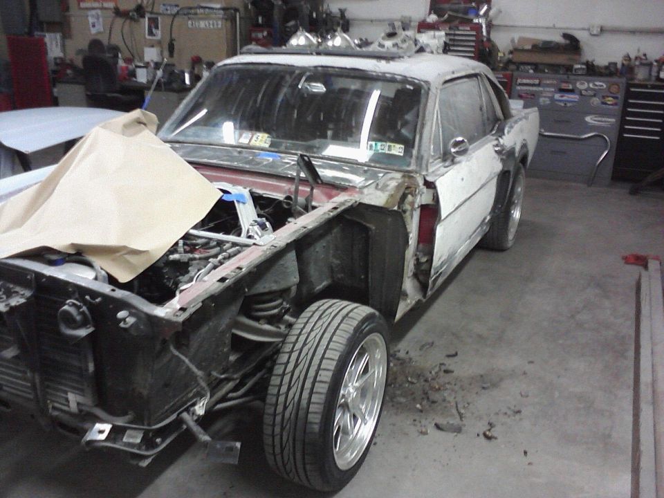 1966 Ford Mustang undergoing restoration, front end disassembled, white body panels, in a garage