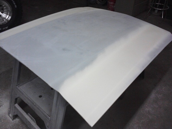 Car hood with primer on a stand, tire visible in upper left