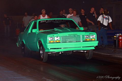 1992 Ford Mustang - A bright green drag car is lined up on a track, with spectators gathered behind it.