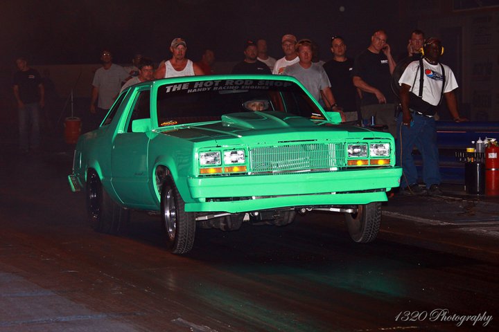 green drag car with hood scoop on track, people watching