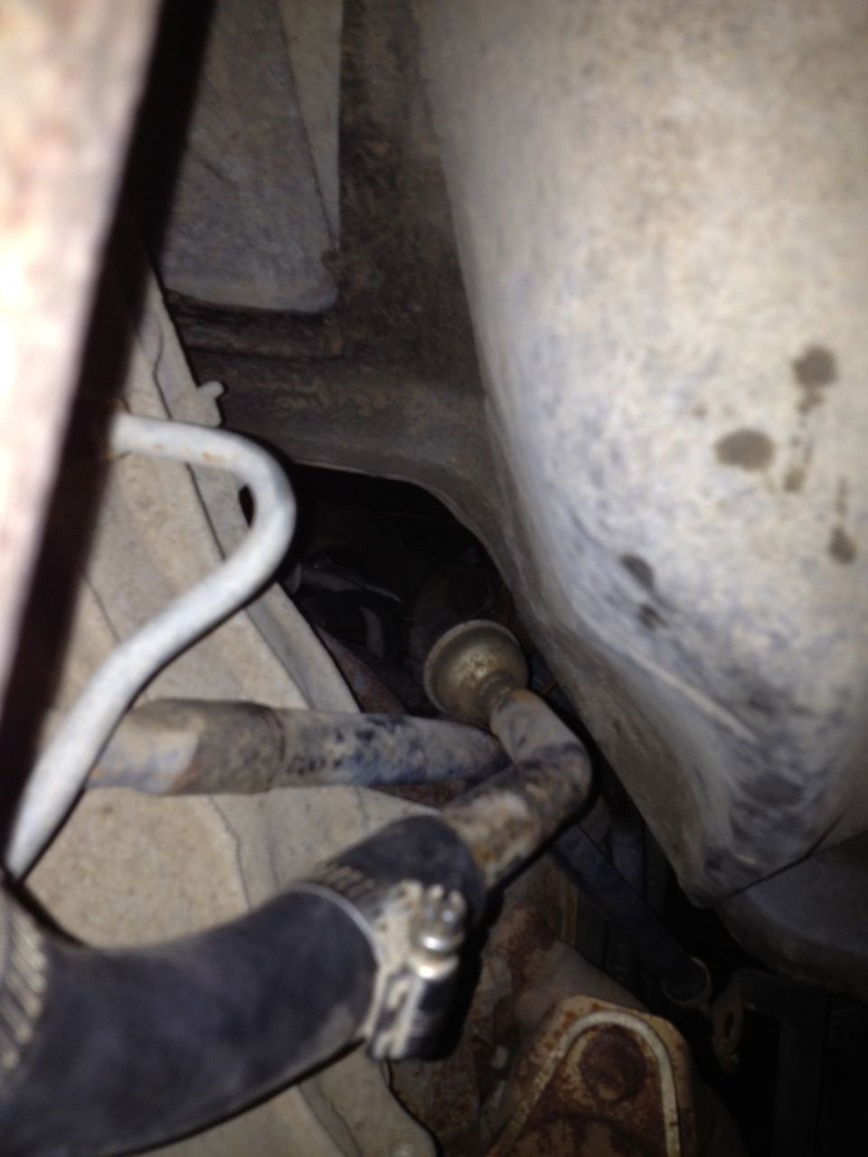 Underside view of vehicle showing rusty hoses, metal lines, and a hose clamp