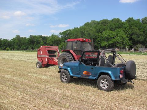 1991 Jeep YJ - A blue 1991 Jeep YJ is parked in a field next to a red tractor and baler on a sunny day.