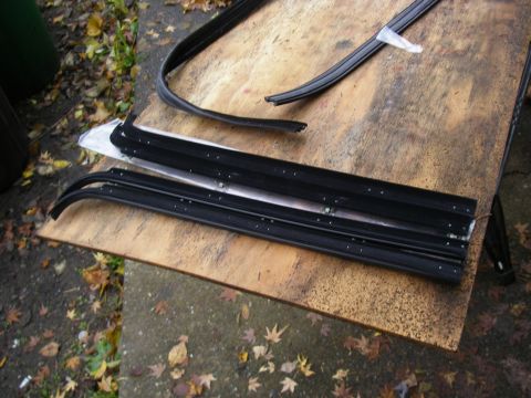 1990 Ford Bronco - Various weatherstripping components are arranged on a weathered wooden surface, with fallen leaves scattered around.