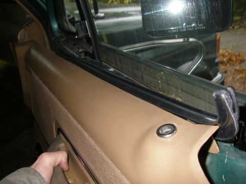1990 Ford Bronco - Interior view of a car door panel and window seal, showing a hand near the door handle.