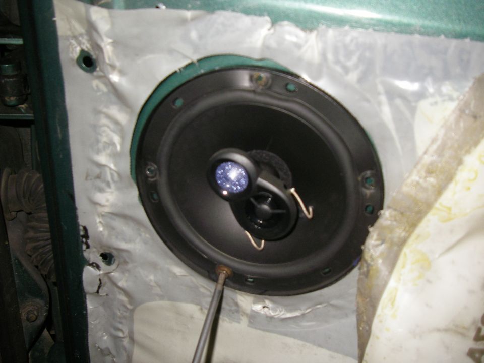 Car door panel with a speaker and tweeter installed. A screwdriver is visible