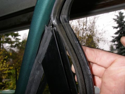 1990 Ford Bronco - Close-up of vehicle weatherstripping and a painted pillar, with trees visible in the background.