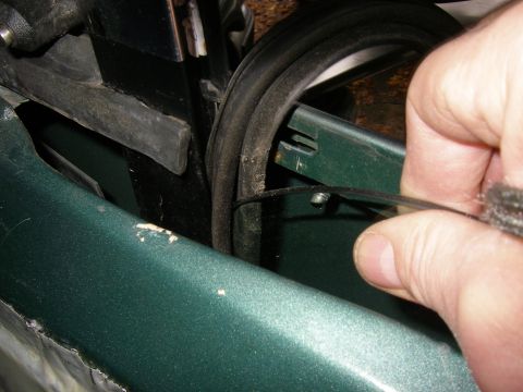 1990 Ford Bronco - A hand adjusts the weatherstripping on a dark green vehicle's door frame.