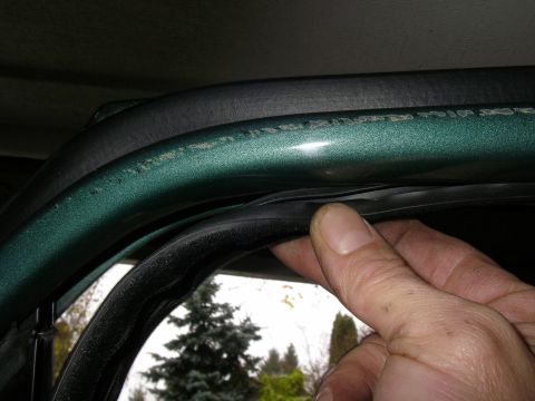 1990 Ford Bronco - Close-up of a car's door seal and frame, with a hand adjusting the weatherstripping.