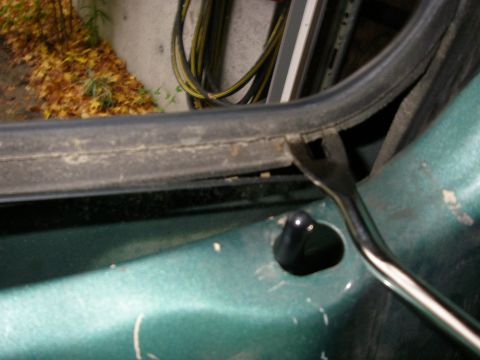 1990 Ford Bronco - A tool is used to remove weatherstripping from the door frame of a green vehicle.