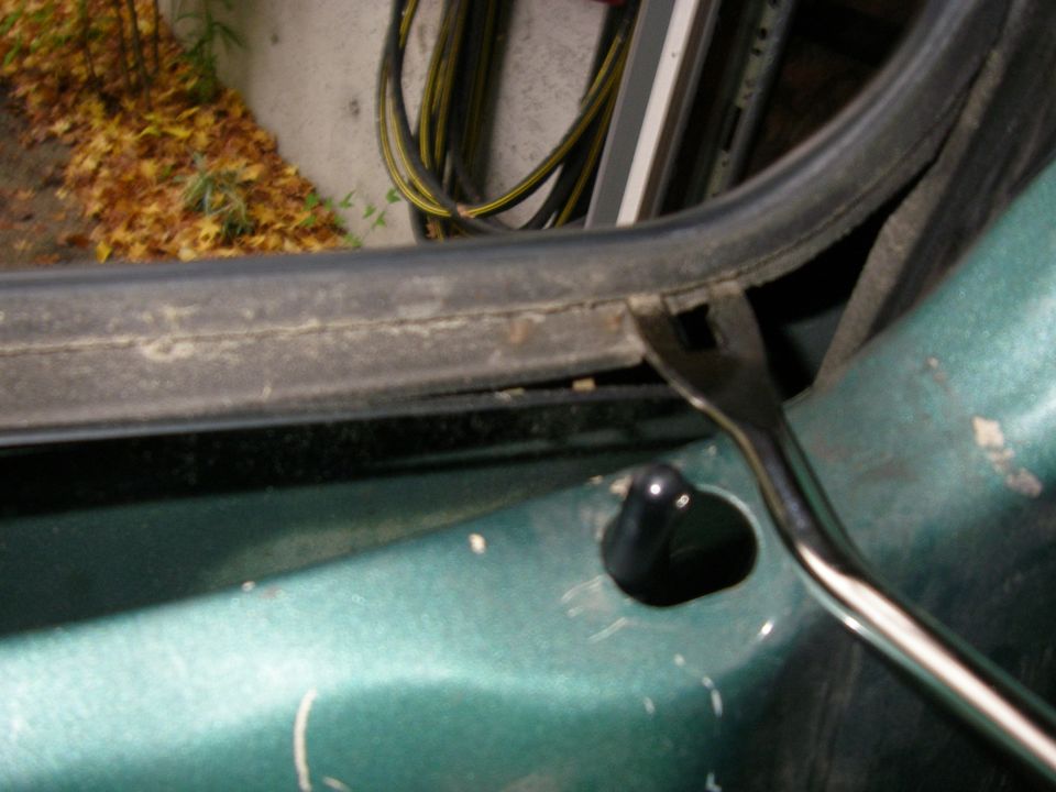 Green car door with weatherstripping being pried off by a tool