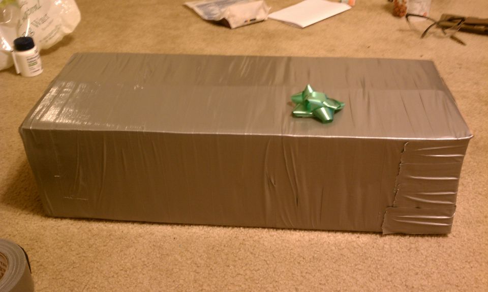 Gray taped box with green bow on carpet, bottle and papers in background