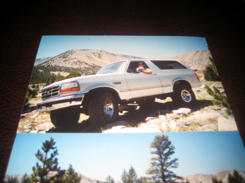 1996 Ford Bronco - A white 1996 Ford Bronco navigates a , rocky mountain landscape under a clear blue sky.