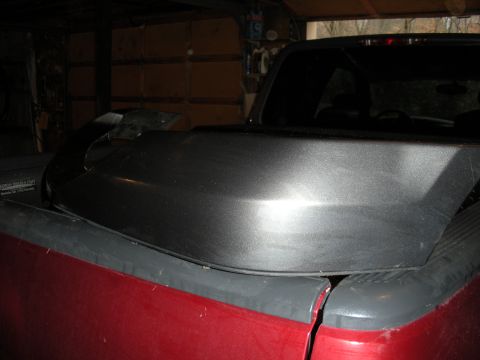 2005 Ford F-250 - A dark gray tonneau cover is installed on the bed of a red pickup truck.
