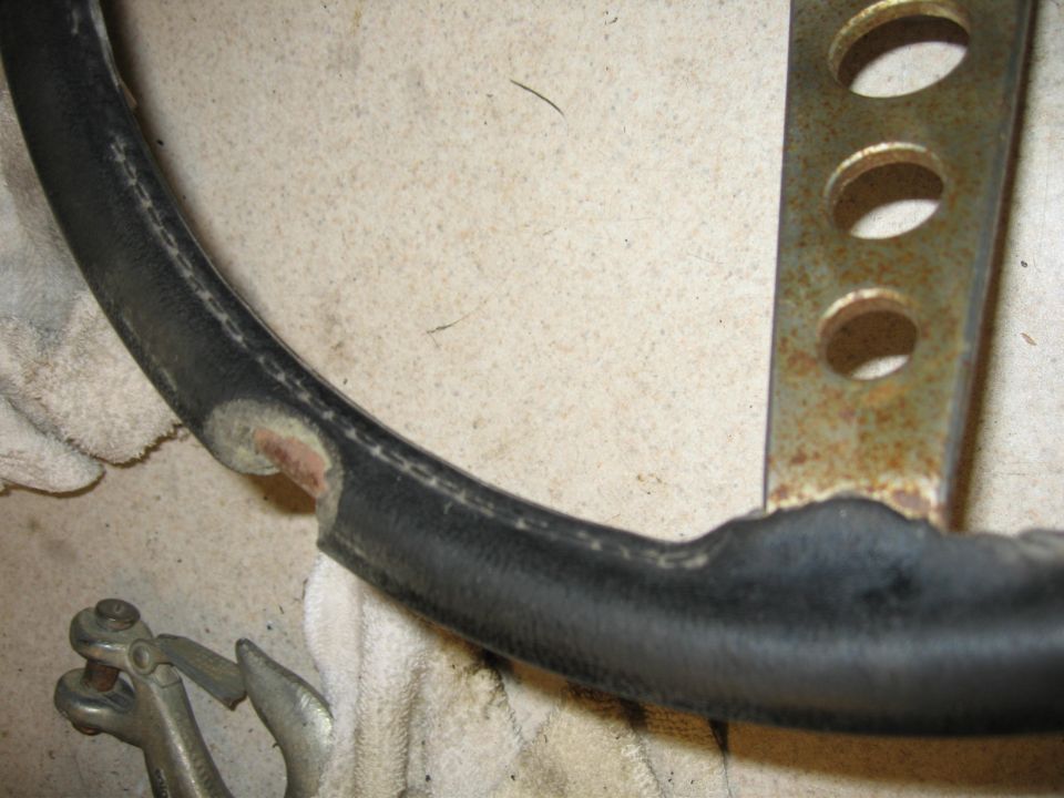 Worn black steering wheel with torn leather and rusted metal spokes
