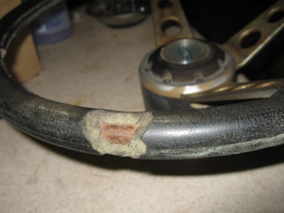 Worn steering wheel with cracked rim exposing foam and core, hub visible behind