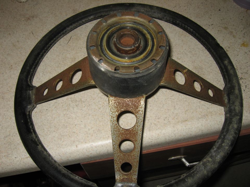 Vintage three-spoke steering wheel with rusty drilled spokes on a counter