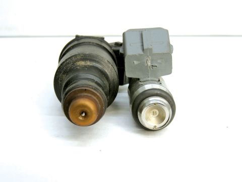 1990 Ford Bronco - Two automotive fuel injectors shown side by side from the nozzle end; the left has a darkened, rubber-booted body with a tan/orange pintle…