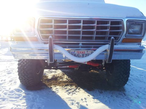 1979 Ford Bronco - Front view of a white 1970s Ford Bronco with chrome bumper and grille, showing a Texas license plate and a coiled white air/tow line draped…