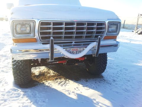 1979 Ford Bronco - Front view of a white 1979-era Ford Bronco with chrome grille and bumper, parked on snow-covered ground. A white U-shaped tube (possibly a…