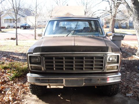1986 Ford Bronco - Head-on front view of a 1980s Ford truck in dark brown, with a 'FORD' lettered grille, dual rectangular headlights, chrome bumper and knobb…