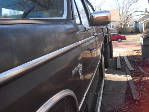 1986 Ford Bronco - Low rear-quarter view down the driver's side of a brown Ford Bronco, showing the BRONCO fender badge, chrome bodyside molding, chrome tubul…