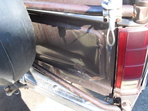1986 Ford Bronco - The rear corner of the truck shows damage to the body panel and a spare tire mounted externally.