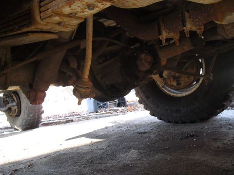 1986 Ford Bronco - The underside of a heavily rusted vehicle, with visible suspension components and tires.