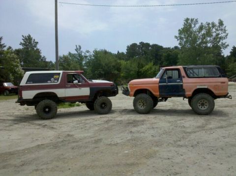 1978 Ford Bronco - Two lifted Ford Broncos, one with a two-tone paint job, are parked facing each other on a dirt surface.
