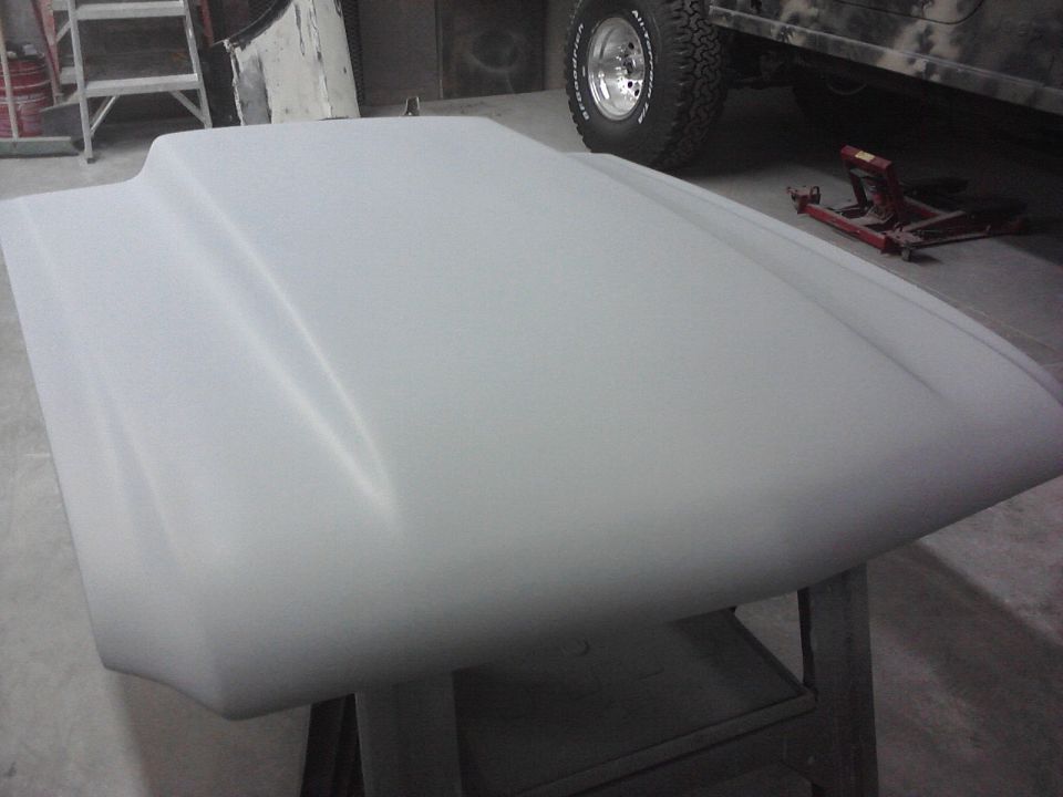 Car hood with a raised center section, sitting on sawhorses. A camouflage Jeep is visible in the background