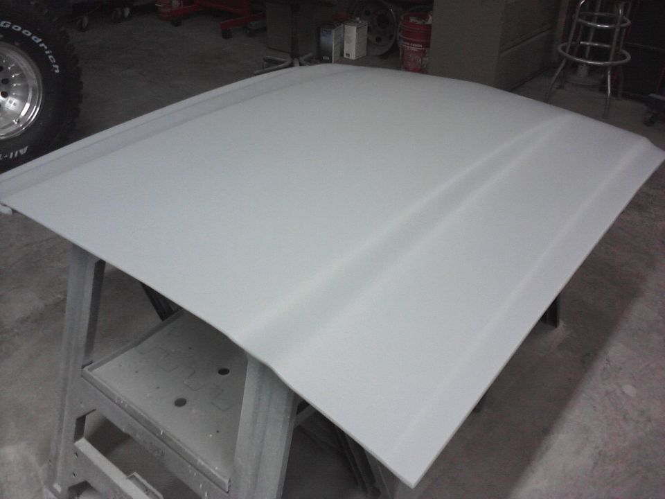 Gray car hood on sawhorses, showing a central raised ridge and a portion of a tire with 'Goodrich' text
