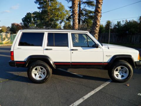 1994 Jeep Cherokee - Side view of a white 1994 Jeep Cherokee parked on asphalt with trees in the background.