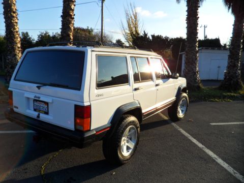 1994 Jeep Cherokee - A white 1994 Jeep Cherokee is parked in a lot, with the sun reflecting off its windows.