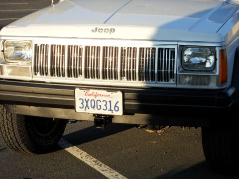 1994 Jeep Cherokee - Front view of a white 1994 Jeep Cherokee, its iconic vertical grille and headlights. The California license plate is clearly visible.