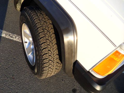 1994 Jeep Cherokee - Close-up view of the front passenger side wheel and fender of a white Jeep Cherokee.